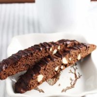 Two chocolate biscotti with almonds on a plate with a cup of coffee