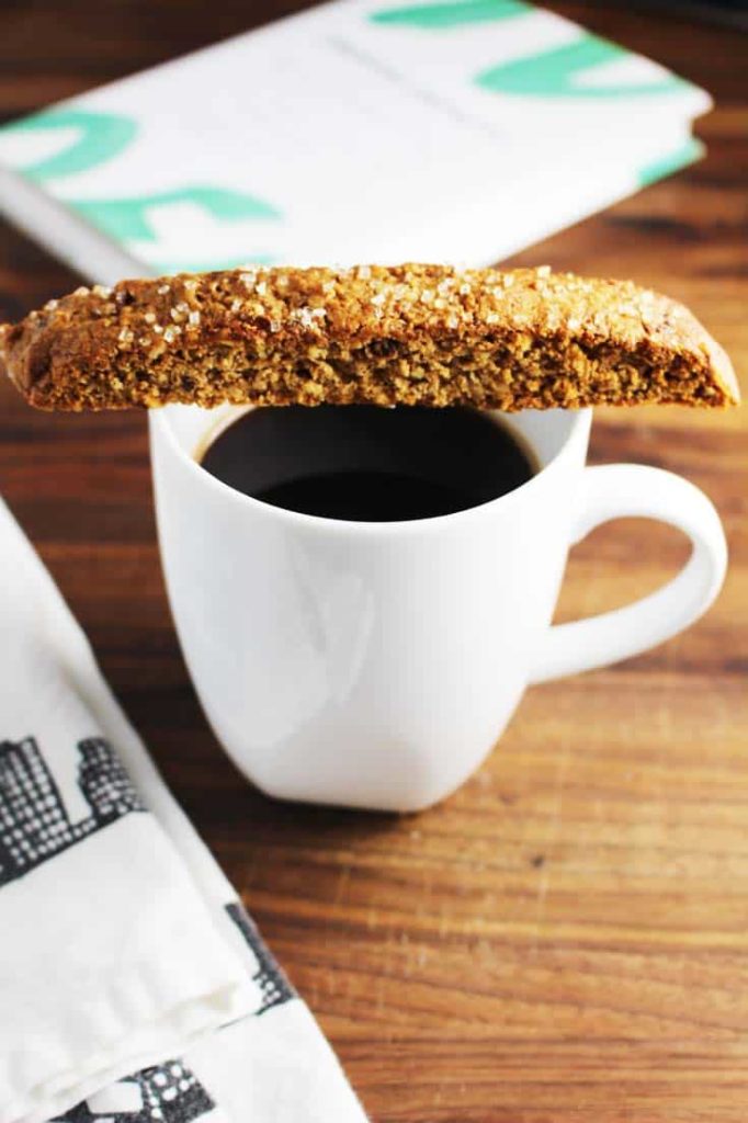 Fig and walnut biscotti laying across the top of a cup of black coffee in a wooden table.