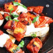 Cheesy caprese chicken in a pan with melted mozzarella, roasted tomatoes and basil