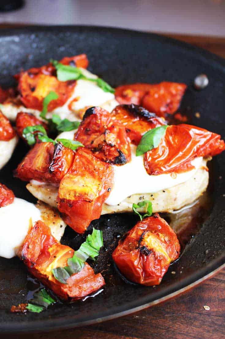 Cheesy caprese chicken in a pan with melted mozzarella, roasted tomatoes and basil
