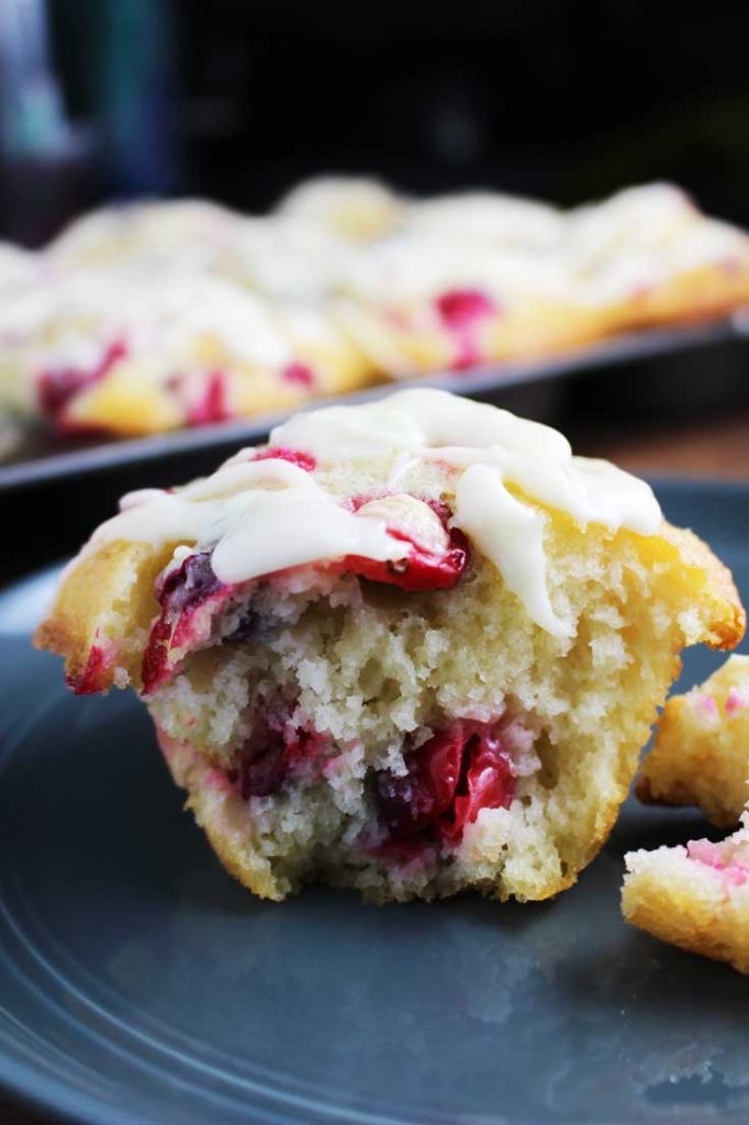 Fresh cranberry orange muffin with a cream cheese drizzle, torn in half and on a plate.