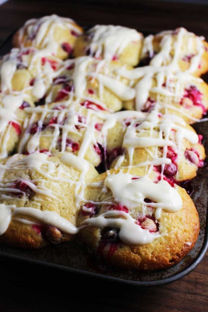 Side view of fresh cranberry orange muffins in muffin pan, drizzled with cream cheese glaze