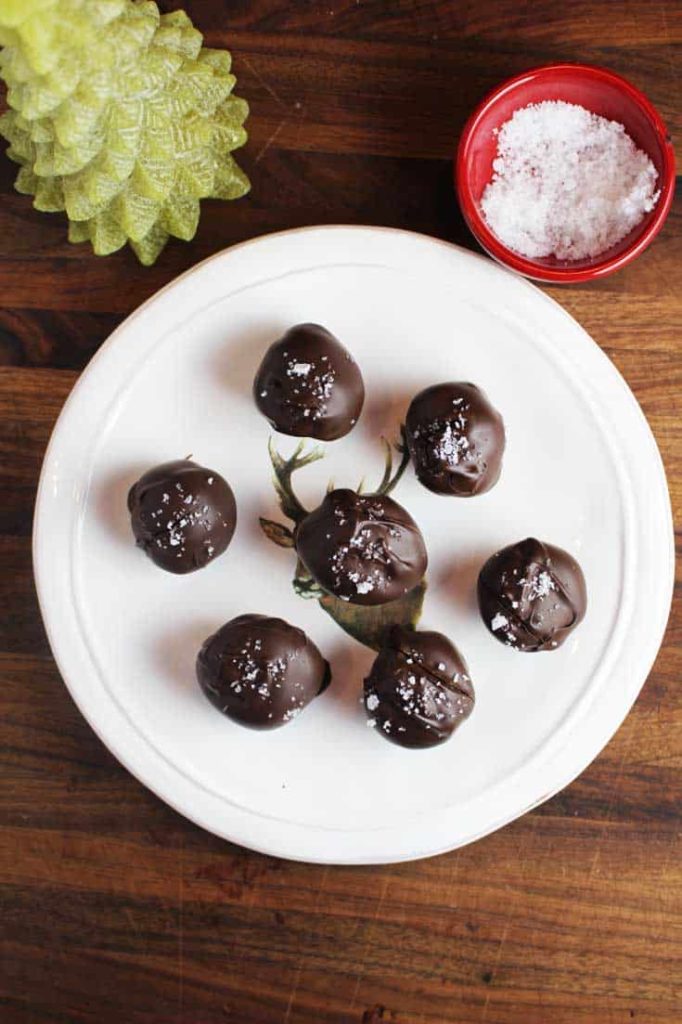 Overhead shot of seven Dark chocolate truffles with caramel, sprinkled with Fleur de sel, on a plate, with a Christmas tree candle in background