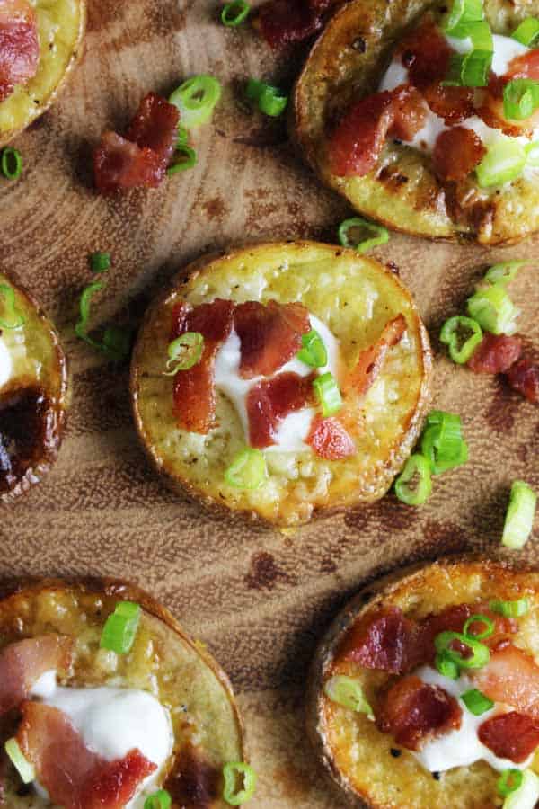 Closeup overhead view of loaded baked potato bites with a dollop of sour cream sprinkled with bacon and chives on a serving platter