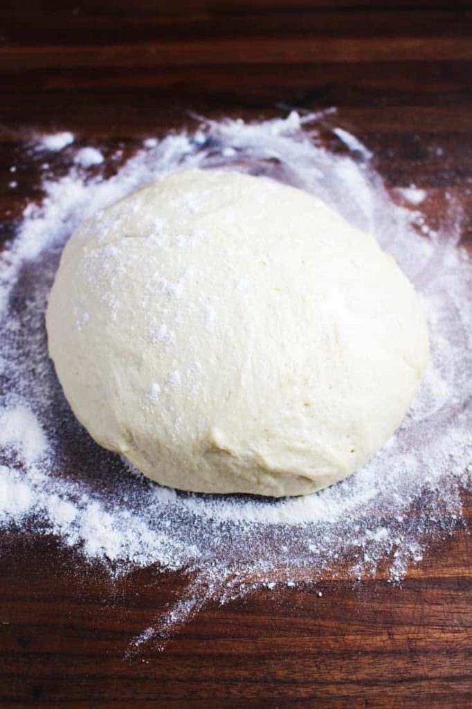 Ball of unbaked pizza dough for a veggie pizza recipe on a floured counter