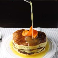 Stack of ricotta pancakes on a plate with orange syrup being poured on top