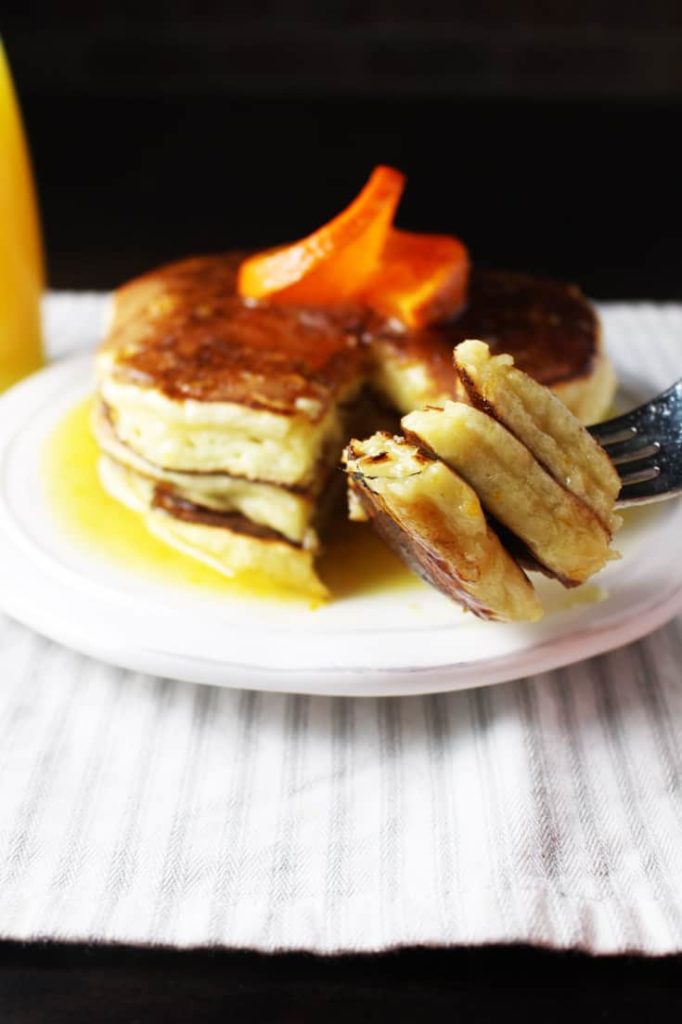 Ricotta pancakes with orange syrup on a plate with a forkful of pancakes in the foreground