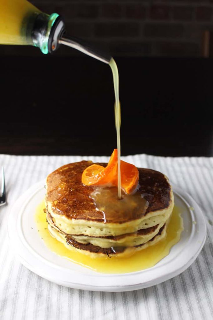 Stack of ricotta pancakes on a plate with orange syrup being poured on top
