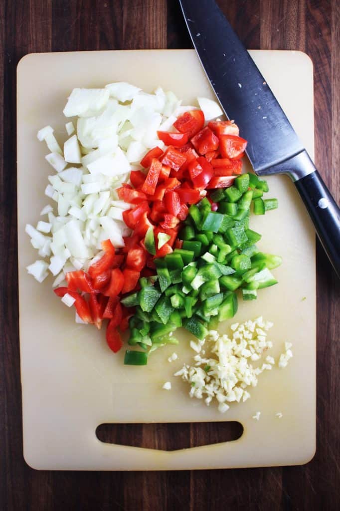 Chopped red and green bell peppers, onions and garlic on a cutting board