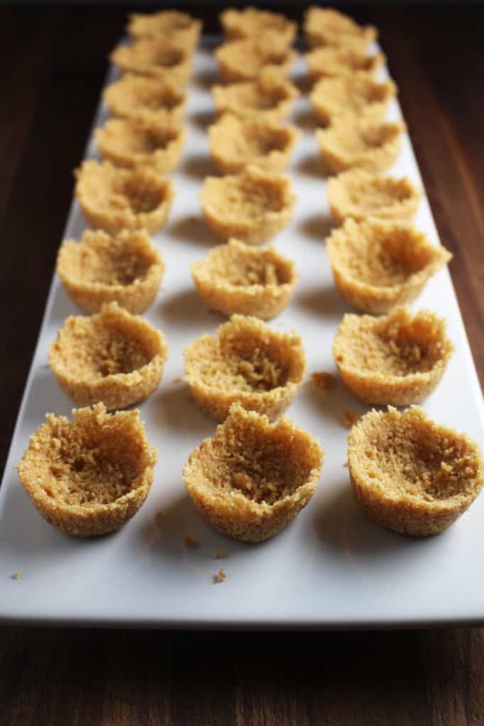 Unfilled graham cracker tart shells for mini cheesecake tarts on a rectangular platter