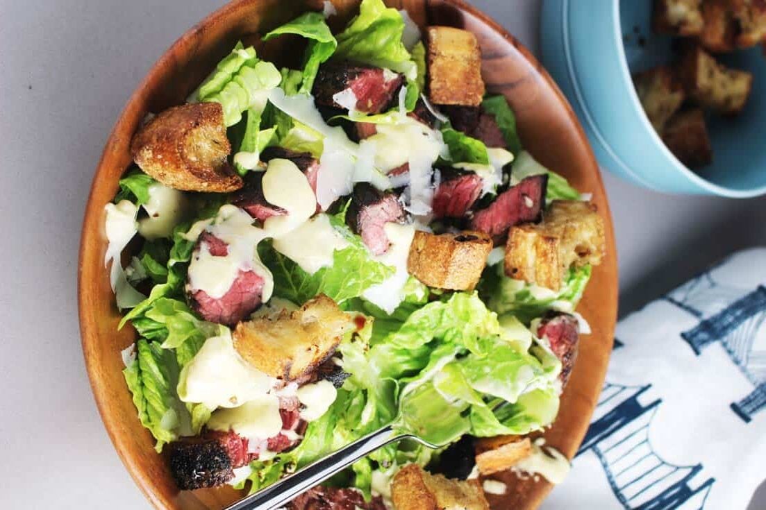 Caesar salad recipe with steak in a wooden bowl