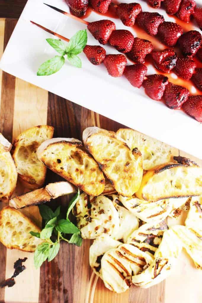 Grilled strawberries on skewers, grilled halloumi and bread on a wooden board