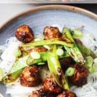 Asian meatballs with honey and sriracha in a bowl over rice noodles and snow peas
