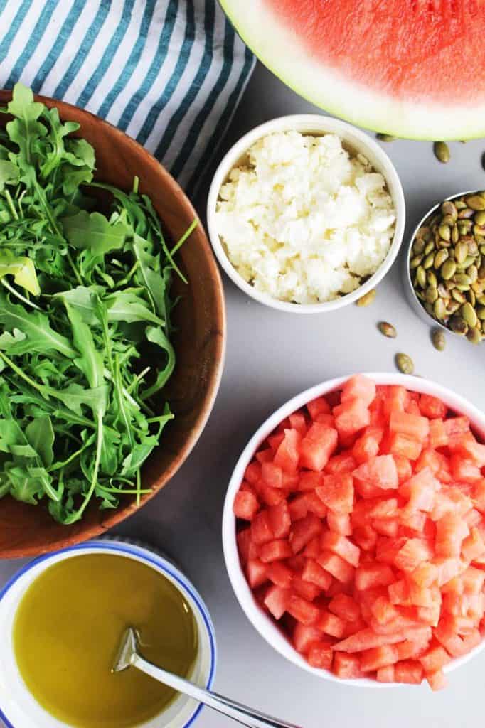 Ingredients in bowls to make watermelon salad with arugula