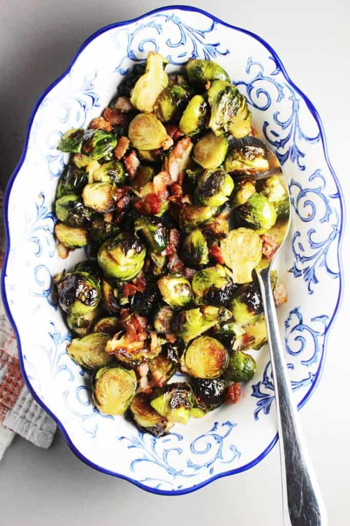 Roasted Brussels Sprouts with maple syrup, balsamic vinegar and bacon in a serving dish with a spoon