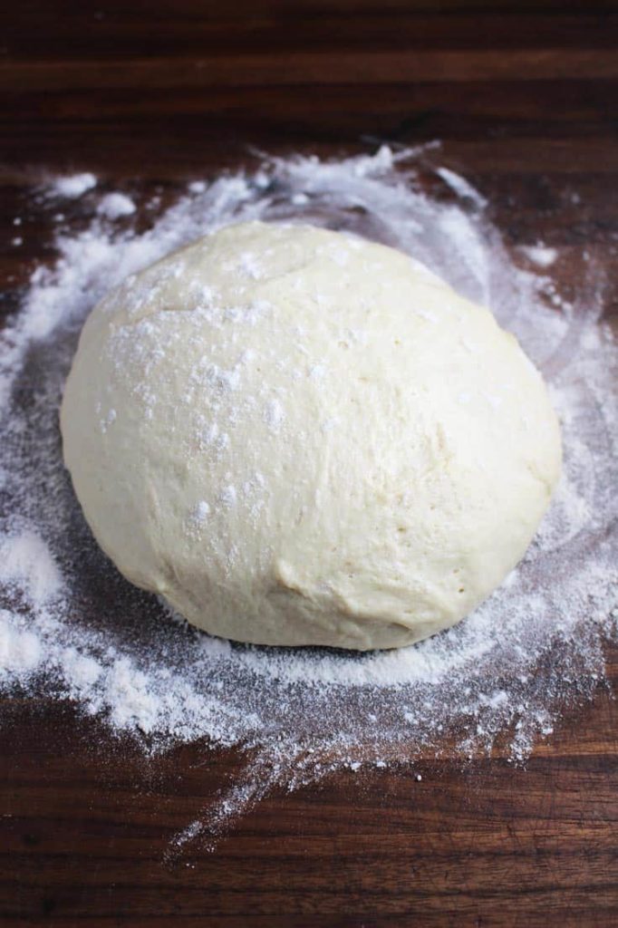 A ball of pizza dough on a floured wood counter