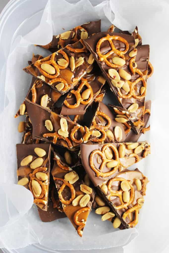 sweet and salty chocolate bark with caramel, peanuts and pretzels in a plastic container with wax paper