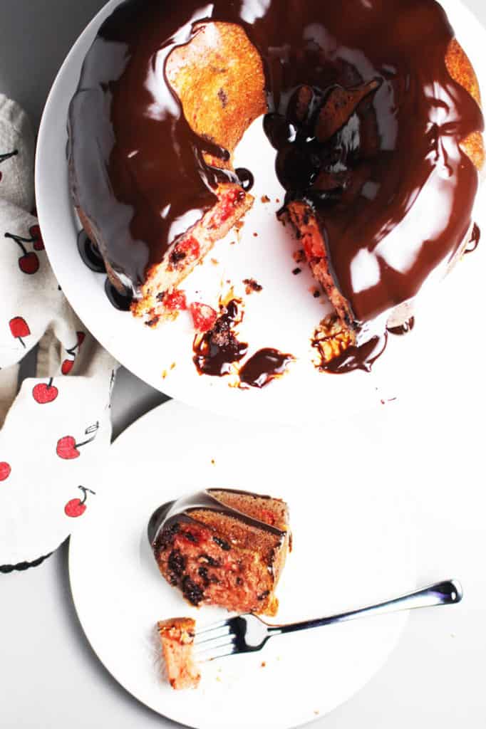 Cherry chocolate cake on a cake stand with a piece of cake on a plate