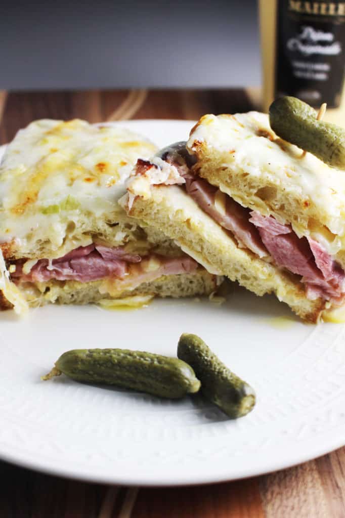 Croque monsieur sandwich sliced in half and served on a plate with a gherkin pickle.