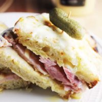 Closeup of a croque monsieur sandwich sliced in half and served on a plate with a gherkin pickle.