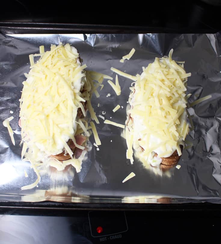 Two croque monsieur sandwiches on a baking sheet, ready to be broiled.