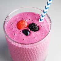 Triple berry Greek yogurt smoothie in a glass with a straw