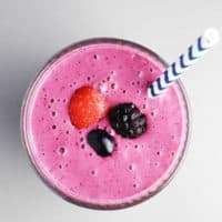 Overhead view of a triple berry smoothie in a glass with a straw garnished with berries