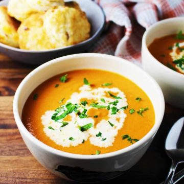 Bowl of tomato soup garnished with cream and parsley, with a bowl of biscuits in the background