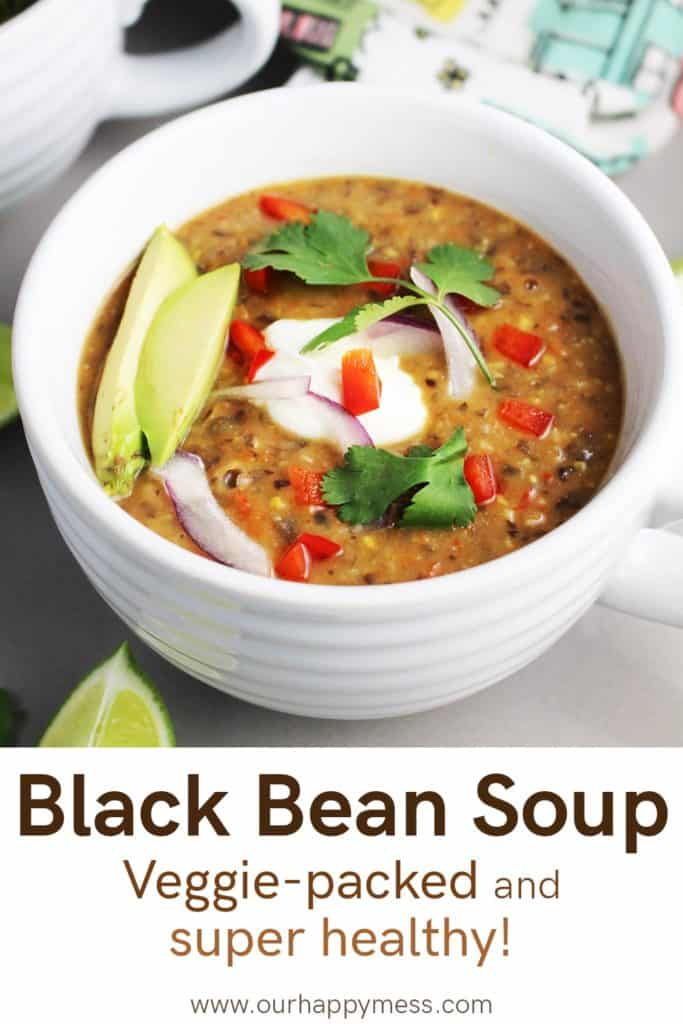 A bowl of vegetarian black bean soup garnished with avocado, sour cream, cilantro, lime and red pepper