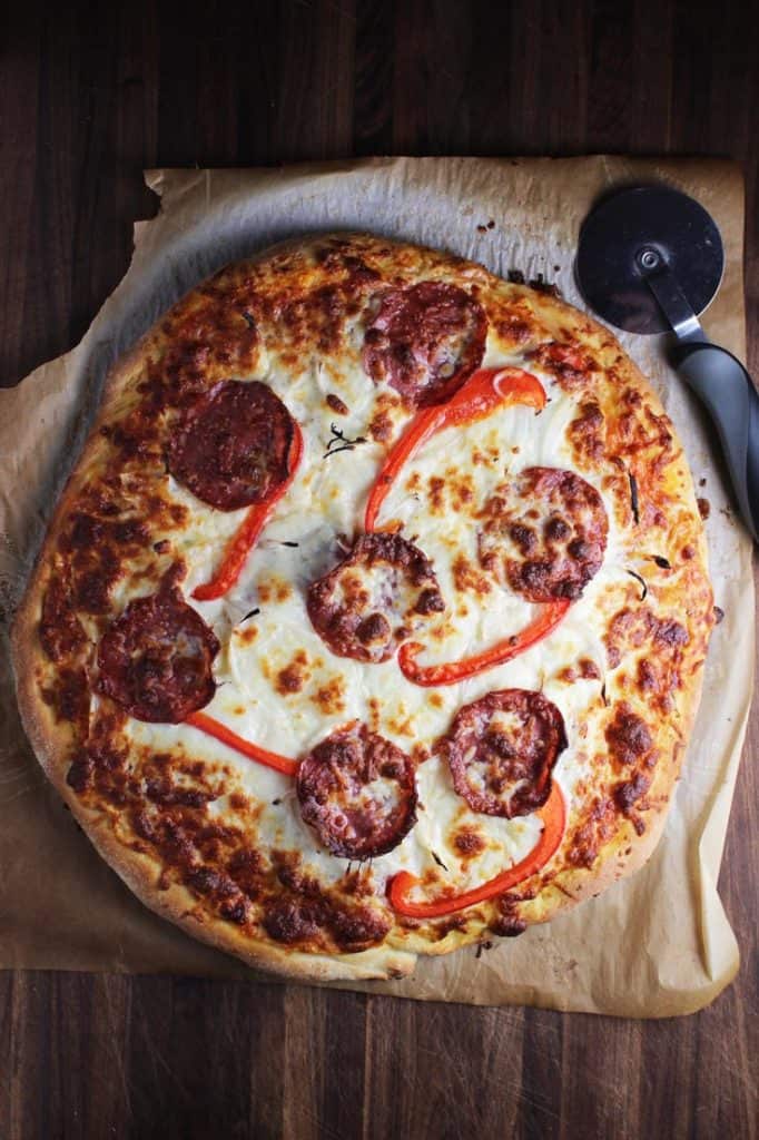 Pepperoni pizza unsliced on a piece of parchment with a pizza wheel