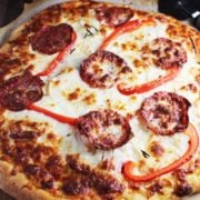 Pepperoni pizza unsliced on a piece of parchment with a pizza wheel