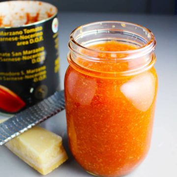 Pizza sauce in a mason jar with parmesan cheese, a microplane grater, and a can of tomatoes in the background