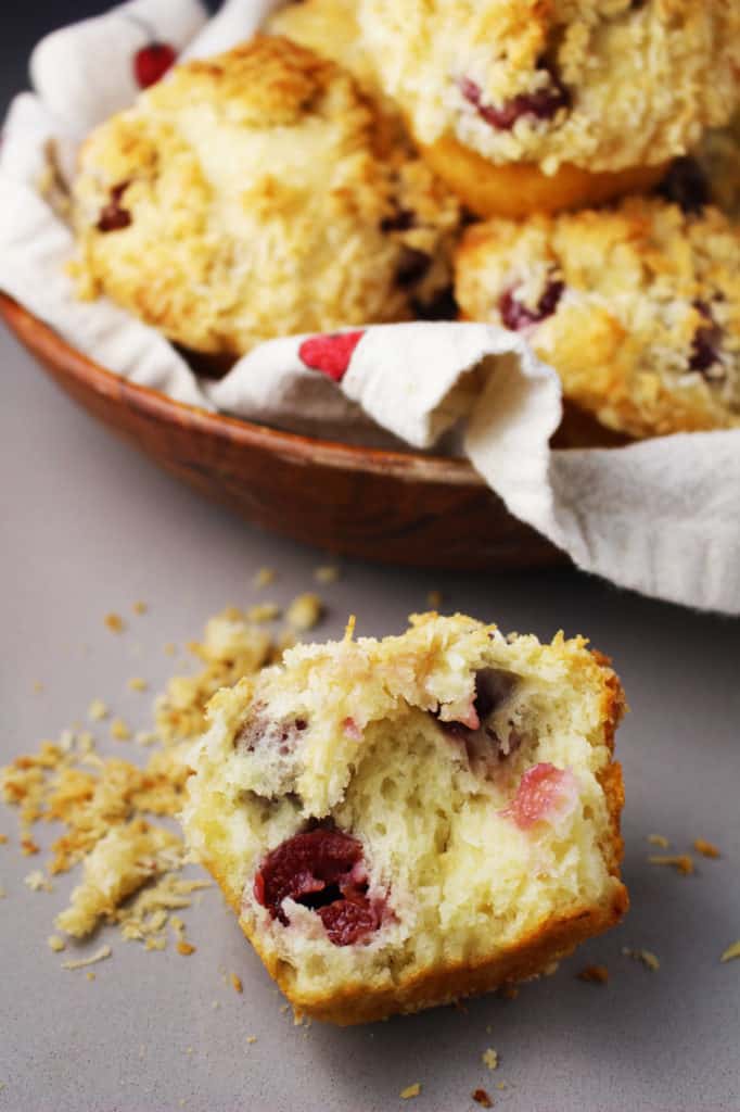 A cherry muffin split in half with a wooden bowl of muffins in the background