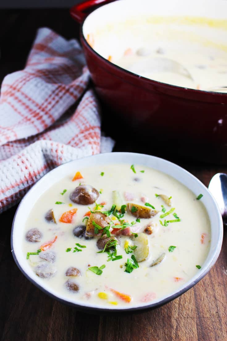 A bowl of potato chowder with corn and ham on a wooden table