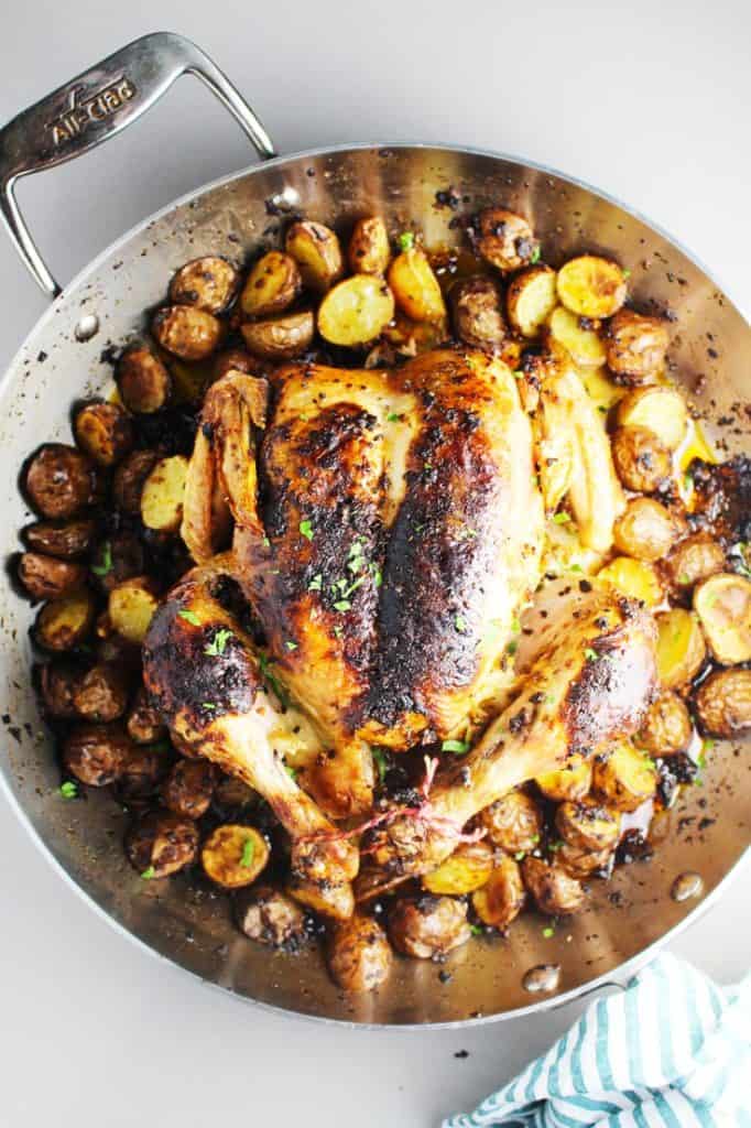 Roasted whole chicken and potatoes with sun dried tomato pest in a pan