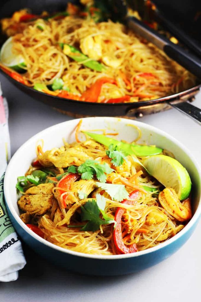 Singapore curry noodles in a bowl garnished with a slice of lime and cilantro