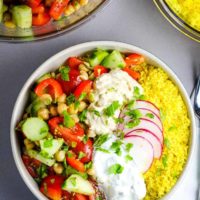 Overhead view of a Mediterranean Buddha bowl with vegetables, couscous, hummus and tzatziki