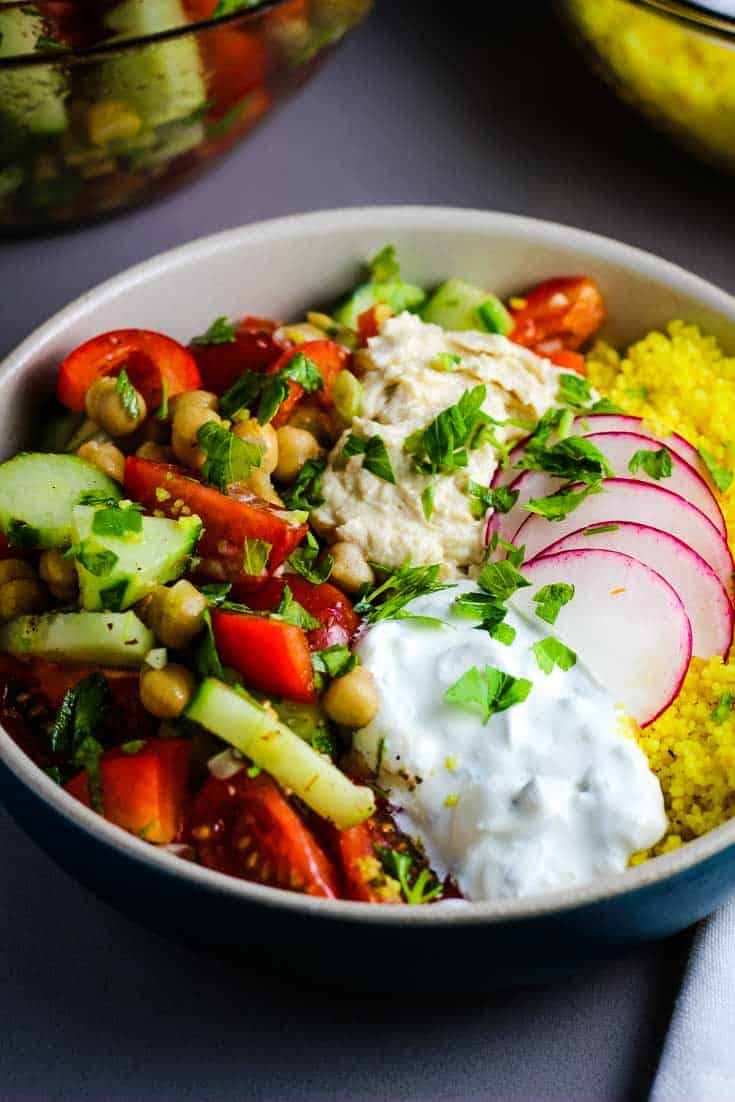 Closeup of a Mediterranean Buddha bowl with couscous, raw vegetables, tzatziki and hummus