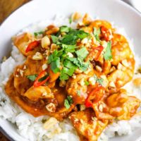 Chicken satay over rice in a bowl garnished with peanuts, cilantro and Thai chiles