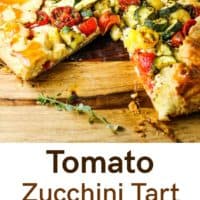 A rustic zucchini tomato tart on a wooden board with a slice taken out