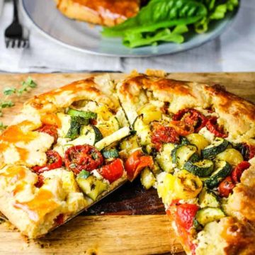 A rustic zucchini tomato tart on a wooden board with a slice take out