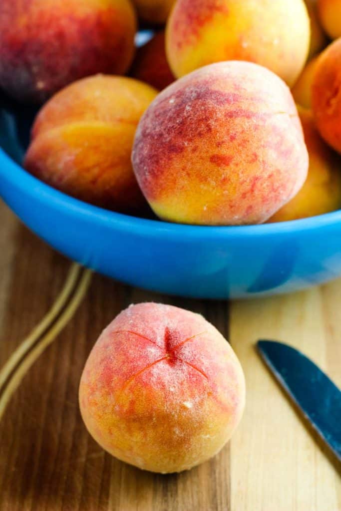 A bowl of peaches, one with an x cut into it for removing the peel