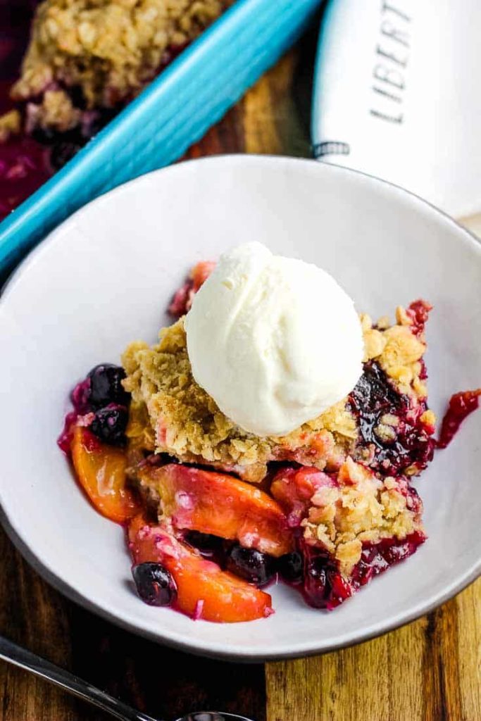 A bowl of blueberry peach crisp with a scoop of vanilla ice cream