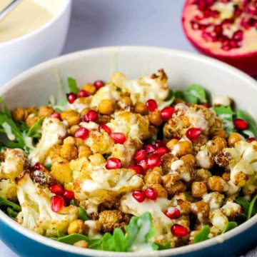 A bowl of roasted cauliflower salad with tahini dressing and pomegranate seeds