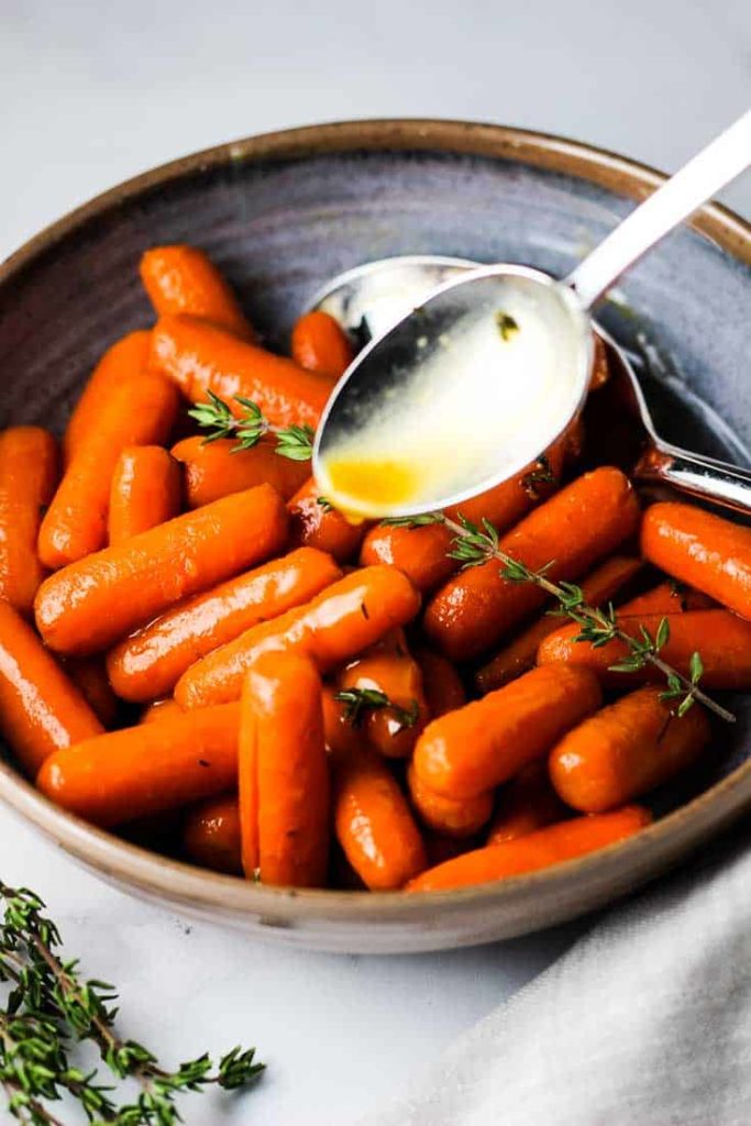 Glazed carrots in a serving bowl with glazed being spooned over them