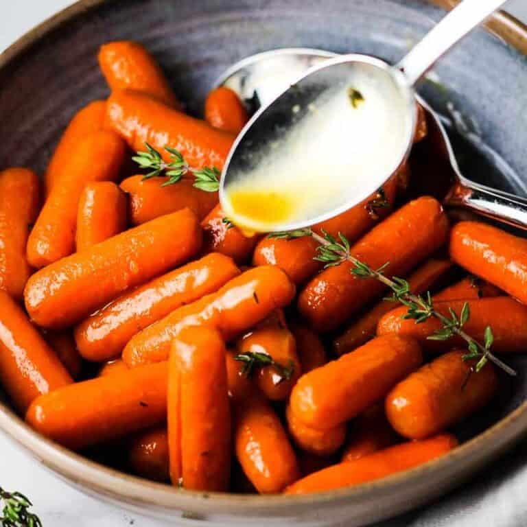 A bowl of brown sugar glazed carrots garnished with thyme.