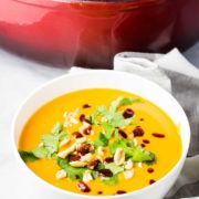 A bowl of sweet potato soup topped with cilantro, peanuts and sriracha