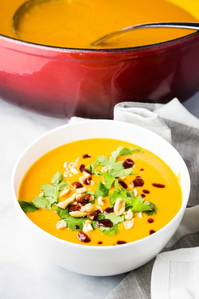 A bowl of sweet potato soup topped with cilantro, peanuts and sriracha