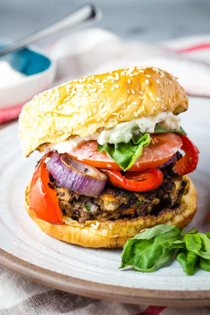 A black bean burger topped with red peppers, onions and basil on a plate