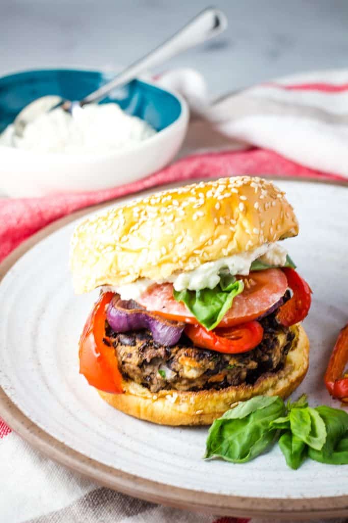 A black bean burger topped with peppers, onions, whipped feta, basil and tomato on a plate